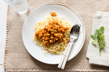 An elegant ceramic dish of bolognese soya meat pasta on a brown tablecloth.
