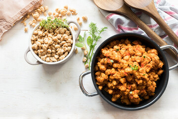 A great bolognese soya meat casserole next to a little white raw soya meta one on a white wooden background.