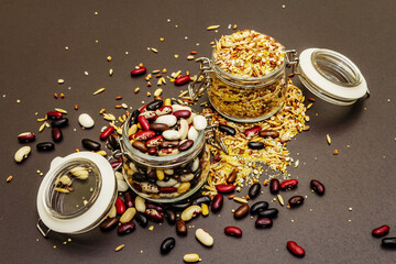 Mix of variety of cereals and beans in glass jars on black stone background
