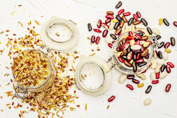 Mix of variety of cereals and beans in glass jars on black stone background