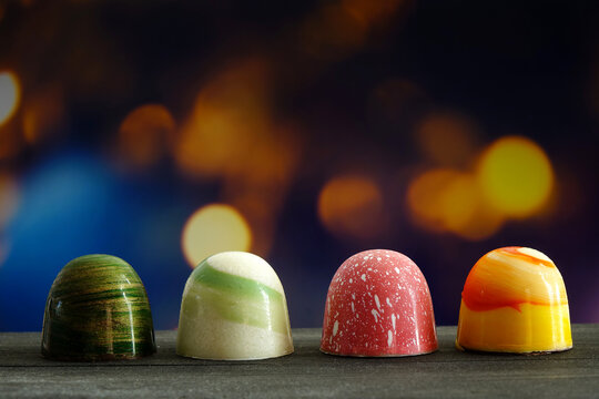 Chocolate bonbon. Luxury handmade chocolate bonbon on wooden table with colorful light night background, copy space. 
