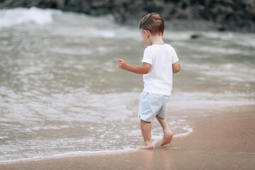 Fototapeta na wymiar rear of little boy in white t-shirt and shorts standing looking the sea
