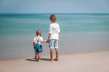 Two brothers relaxing on the beach of the sea.The little boy is holding the hand of his older brother.