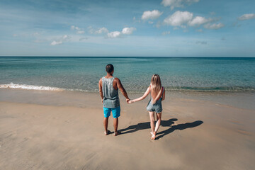 happy young couple walking, blonde girl and a man, having fun on the beach. Phuket. Thailand. Back view