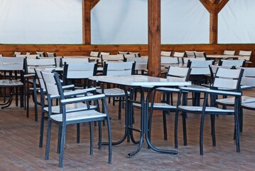 white black wooden tables and chairs stand on a brown sidewalk in an open veranda of a restaurant on the street