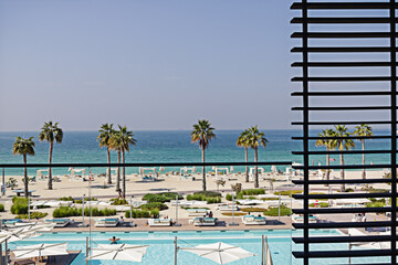 Wonderful balcony view on a seashore and a pool with palm trees on a sunny day