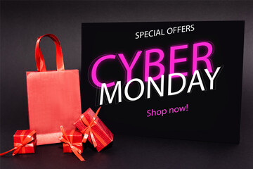 red presents and shopping bag near placard with special offers, cyber monday, shop now lettering on dark 