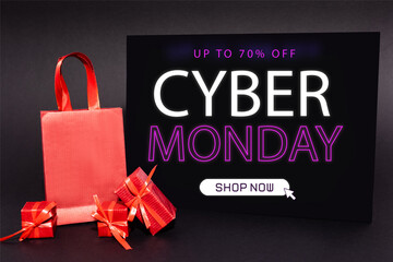 presents and shopping bag near placard with up to 70 percent off, cyber monday, shop now lettering on dark background