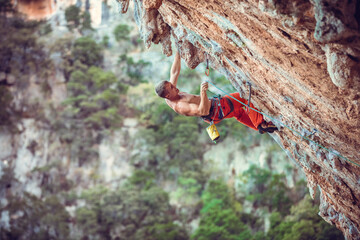 Rock climber clipping rope while climbing challenging route on cliff