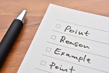 A piece of paper with a checklist labeled "Point, Reason, Example, Point" sits on top of the notebook.
