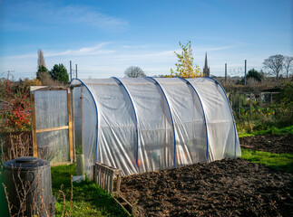 Outdoor transparent pvc greenhouse with open door 
at the foot of plowed and sown land on a sunny day.