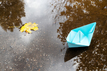one blue paper ship floating on a water surface. outdoors. autumn season. greeting card with copy space. leadership conceptual. freedom concept