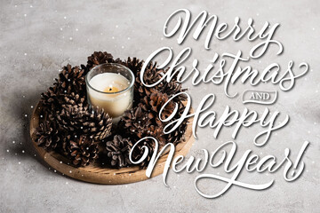 Scented candle with pine cones on wooden plate near merry christmas and happy new year lettering on grey 