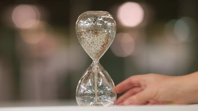Let the countdown to Xmas begin. Isolated object on gray blurred background. The hourglass is turned over by the hand, symbol of transience time begins to run. Waiting for the holidays.