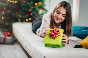 A cheerful girl opens a gift at the Christmas tree.