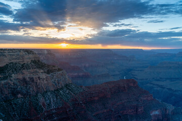 sunset shot of sunbeams extending upwards from behind clouds at hopi point of the grand canyon national park in arizona