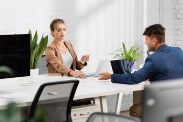  executive giving document to colleague, while sitting at table with plants in office