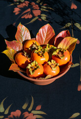 An earthenware bowl of ripe Fuyu persimmons and persimmon leaves in autumn colors