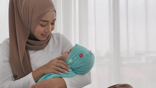A young Muslim mother smiles and happy to look at the face of her baby daughter is sleeping in her embrace. She uses the thumb with a soft touch on the  face of her infant.