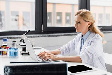scientist using laptop near microscope and devices in lab, stock image