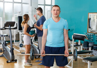 Fototapeta na wymiar Young man in sportswear doing exercises with barbell in gym