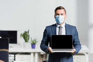 Front of businessman holding laptop with blank screen with blurred office on background