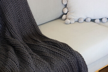 A knitted grey throw rug on a sofa.