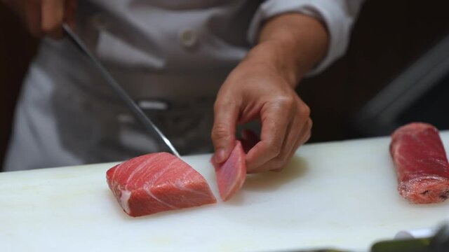 Close up of Professional male chef hand using fish fillet knife slice fresh red tuna meat on cutting board in restaurant kitchen. Chef preparing healthy menu salmon sashimi or sushi to customer
