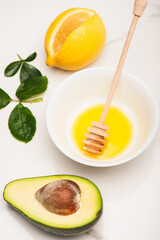Fresh juicy avocado, lemon, bowl with honey and wooden spoon near rose leaves on white, stock image