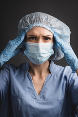 nurse in medical cap and mask suffering from headache isolated on dark 
