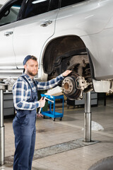  mechanic looking at camera while standing near auto, raised on car lift