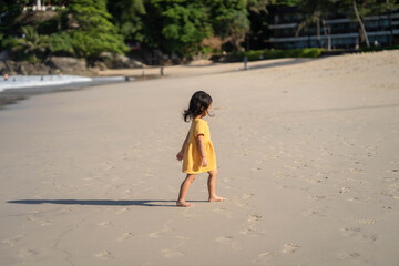 little girl in yellow dress walking at sea shore.