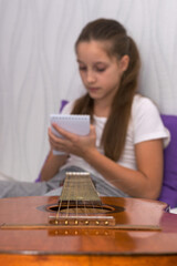The girl takes online guitar training on a laptop and makes notes in a notebook.