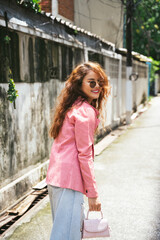 Fashion portrait of asian woman wearing sunglasses and pink jacket on street.