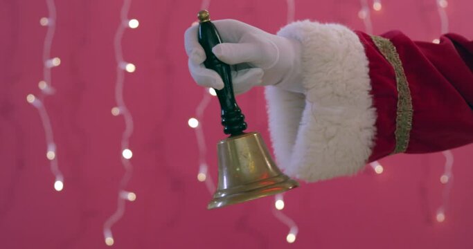 Santa's hand and arm with white glove  ringing a jingle hand bell on pink background at Christmas