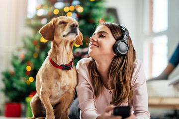 A teenage girl listens to music while lying on the floor with her dog near the Christmas tree