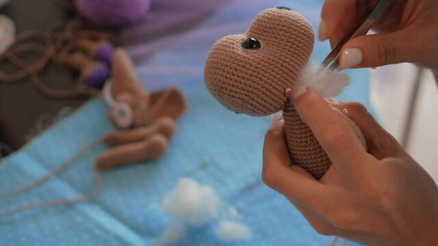Young woman fills with cotton wool toy. Knitting hand made hobby Close-up of woman's hands with brown knitted toy dog