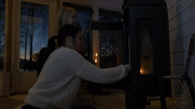 Caucasian mother and young daughter light wood burning stove indoors