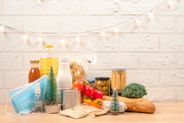 Christmas donation box - food donations on light background with copyspace - pasta, fresh vegatables, canned food, baguette, cooking oil with Christmas decorations. Food bank, selective focus