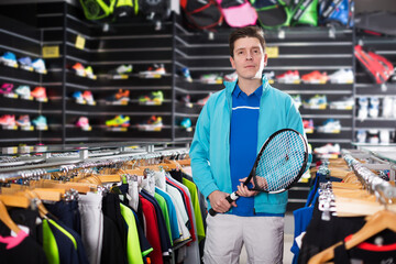 Tennis male is standing in uniform with new tennis rocket in the speciality store