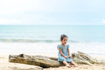 Fototapeta na wymiar little girl sitting on timber at the beach against blue sky.