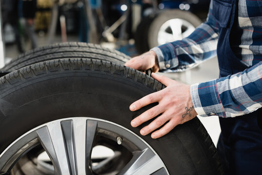 cropped view of technician moving car wheel in workshop, stock image