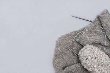 grey knitting yarn in a skein with needles and a scarf on grey background. monochrome trendy image. relaxing hobby and leisure for everybody. wool yarn for winter handmade clothes.