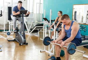 Young man in sportswear doing exercises with barbell in gym