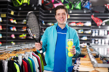 Fototapeta premium Male is standing in sport uniform with new tennis rocket and balls in the speciality store