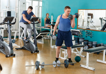 Fototapeta na wymiar Cheerful sporty guy doing exercises with dumbbells at gym