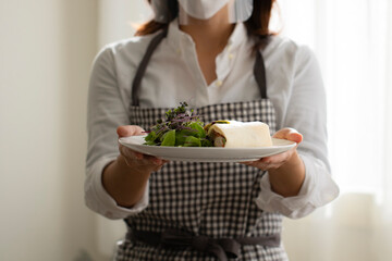 マスクとフェイスガードをつけて料理を運ぶ女性