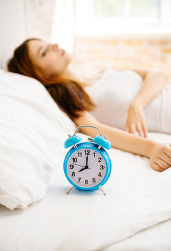 Image of woman waking up at bedroom, with alarmclock. Brunette girl in domestic life and leisure concept.