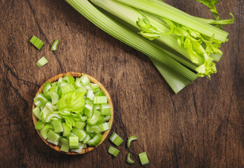 Green celery chopped pieces in bowl, wooden table, top view, copy space