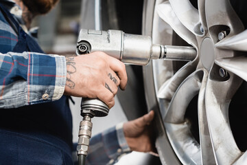 cropped view of mechanic fixing car wheel with pneumatic wrench on blurred 